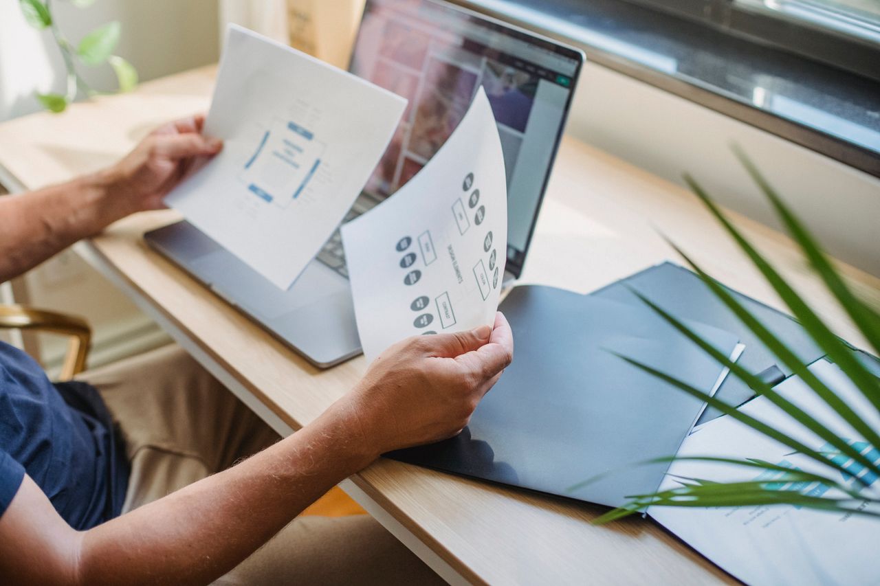summer-sale Crop anonymous male designer in casual wear sitting at table with opened laptop and folders and reading papers